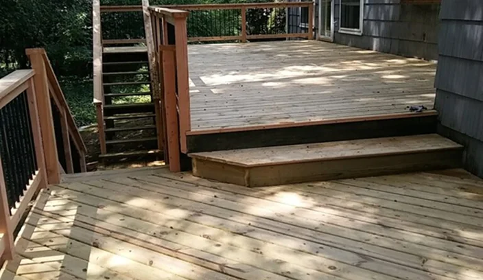 Repaired wooden deck with newly installed boards and steps attached to a house.
